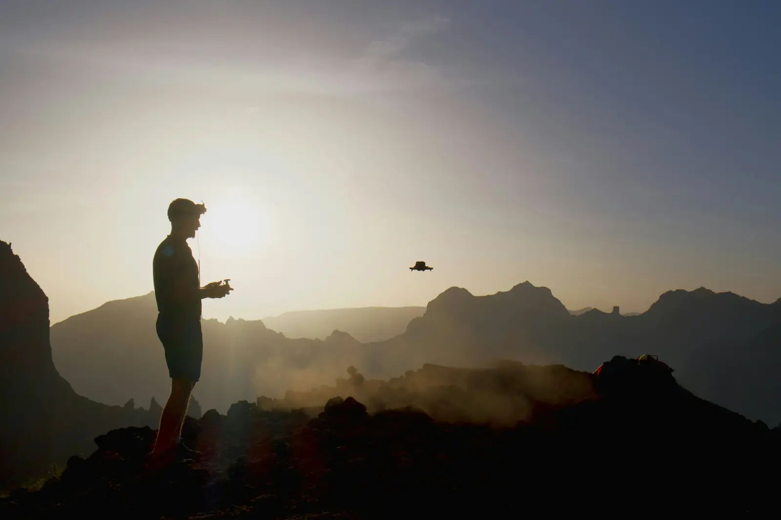 A person flying a drone on a hilltop at dusk