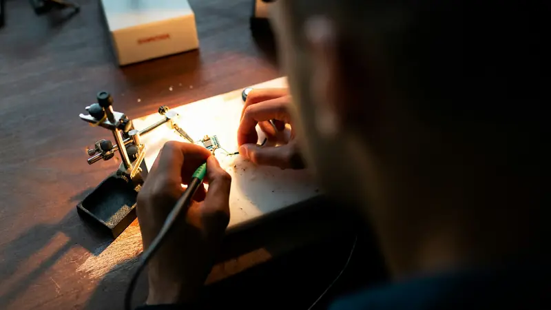 An engineer soldering a circuit board under a work lamp