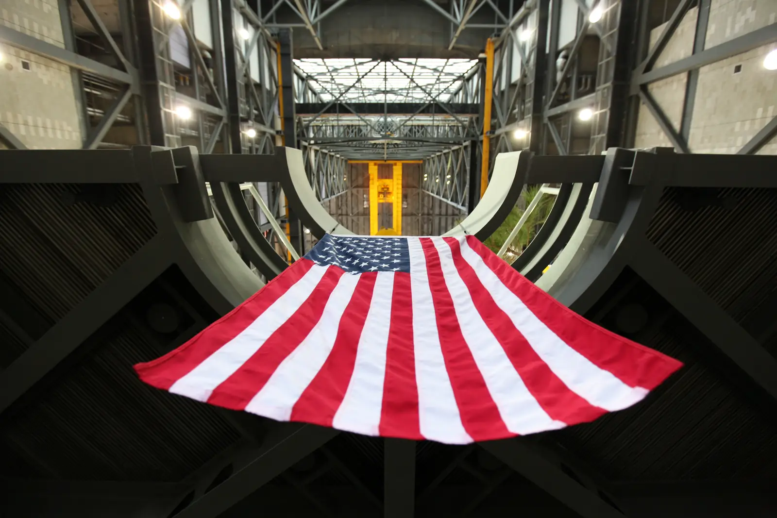 A large American flag hanging from a steel work platform in a tall assembly hall