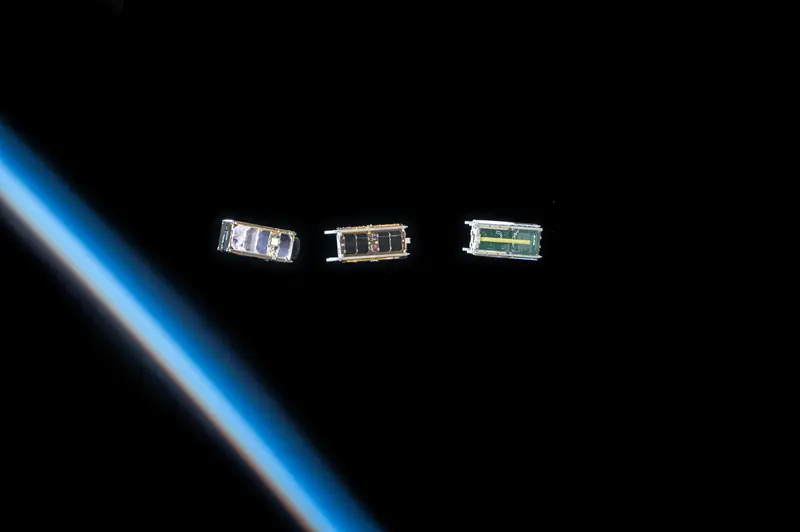 Three small satellites just released into orbit, above the thin blue line of the Earth’s atmosphere