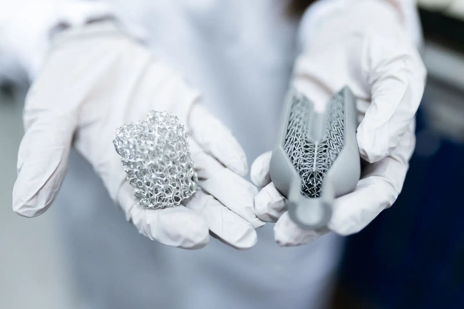 Gloved hands holding 3D-printed metal lattice parts