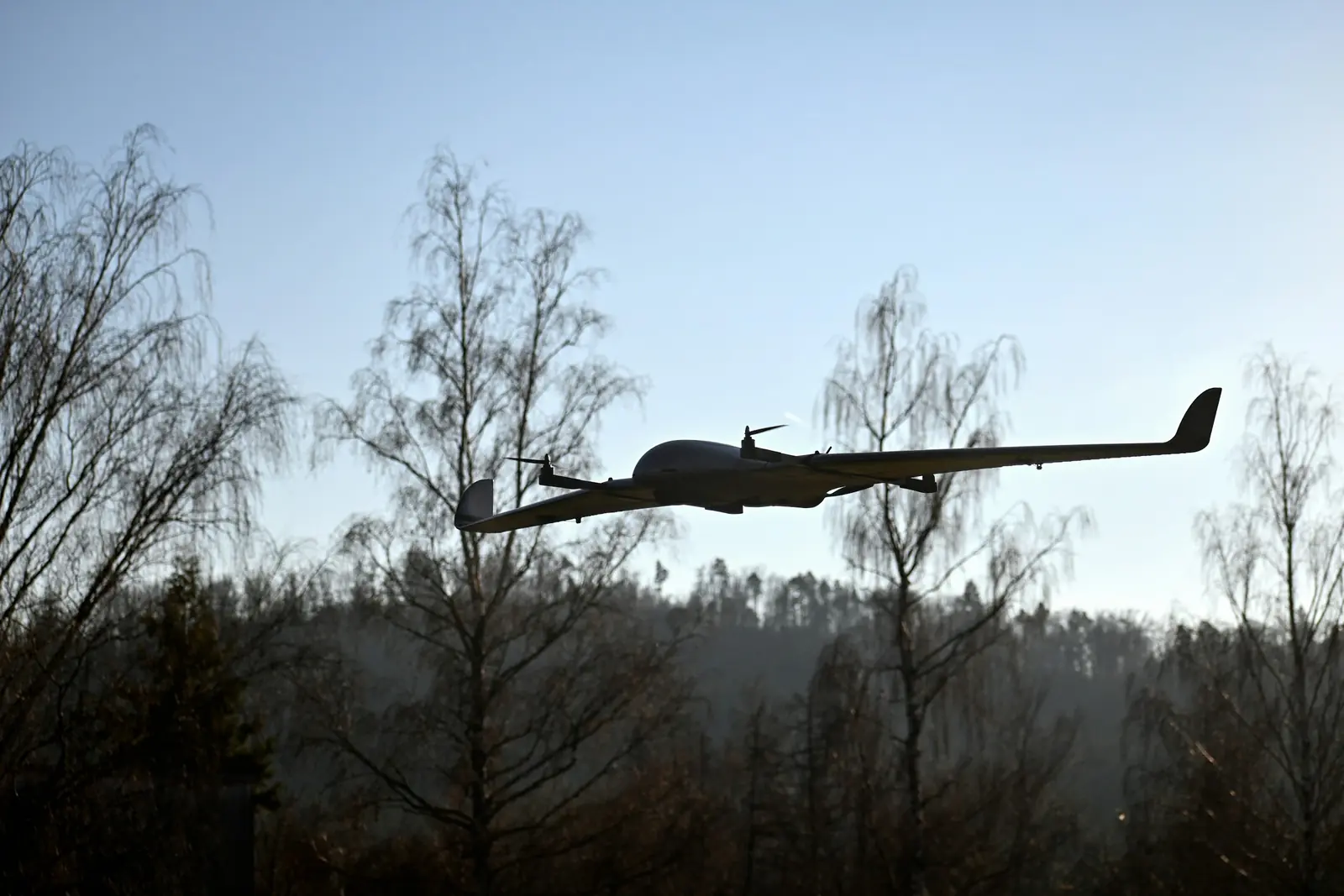 A fixed-wing drone flying low over a forest